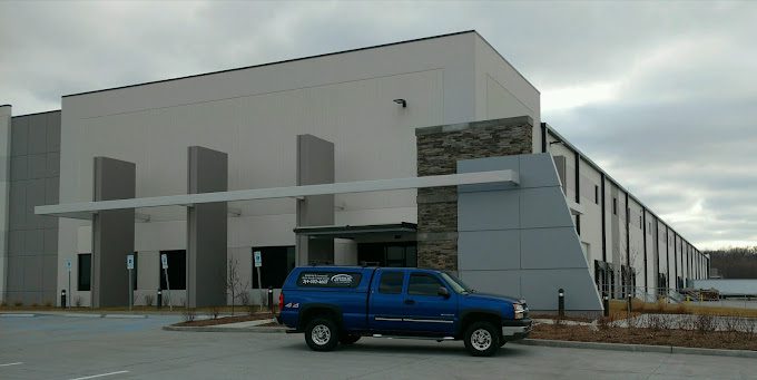 Blue truck parked outside large industrial building.